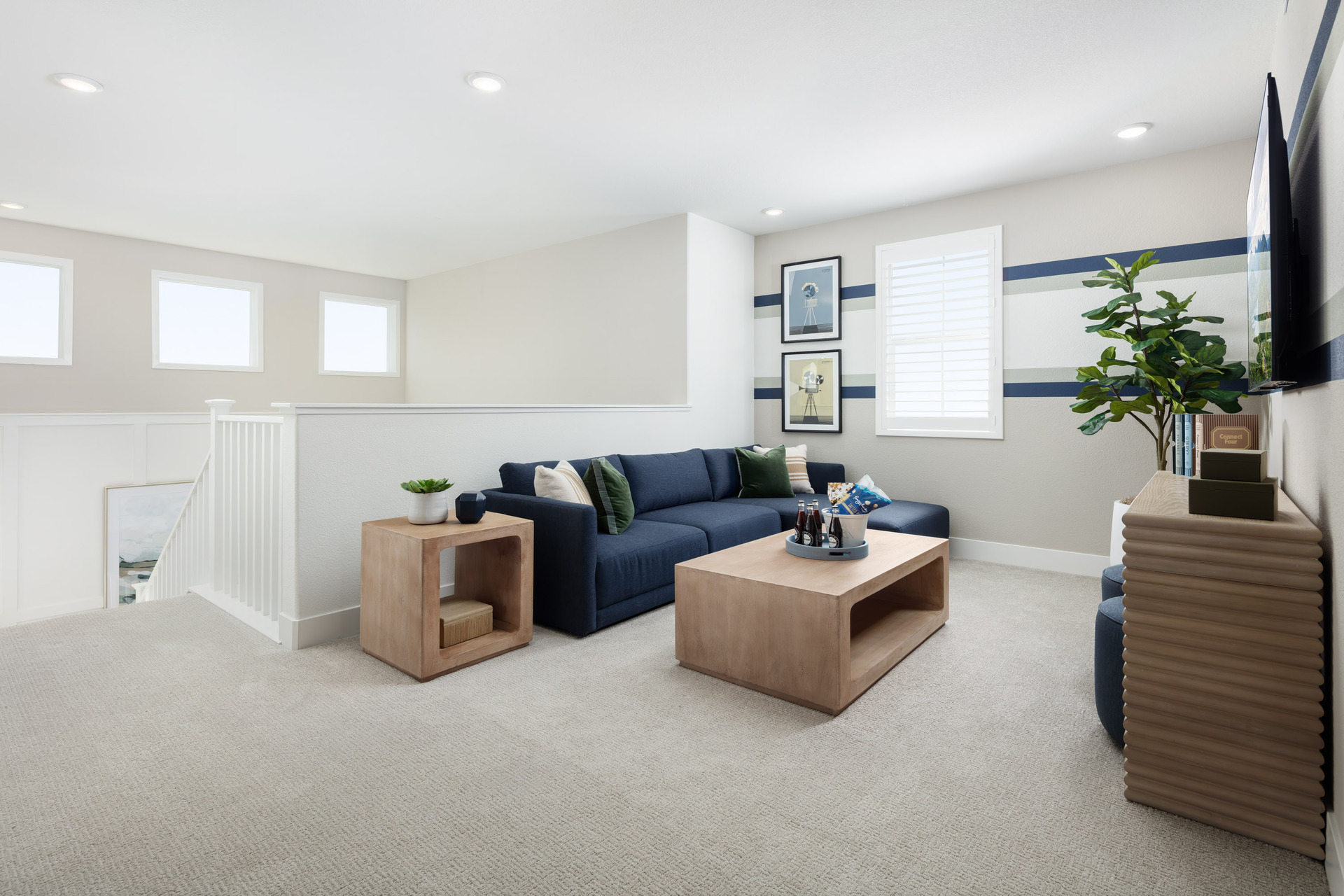 loft with navy blue sofa, light wood tables, multiple windows, and plant in corner