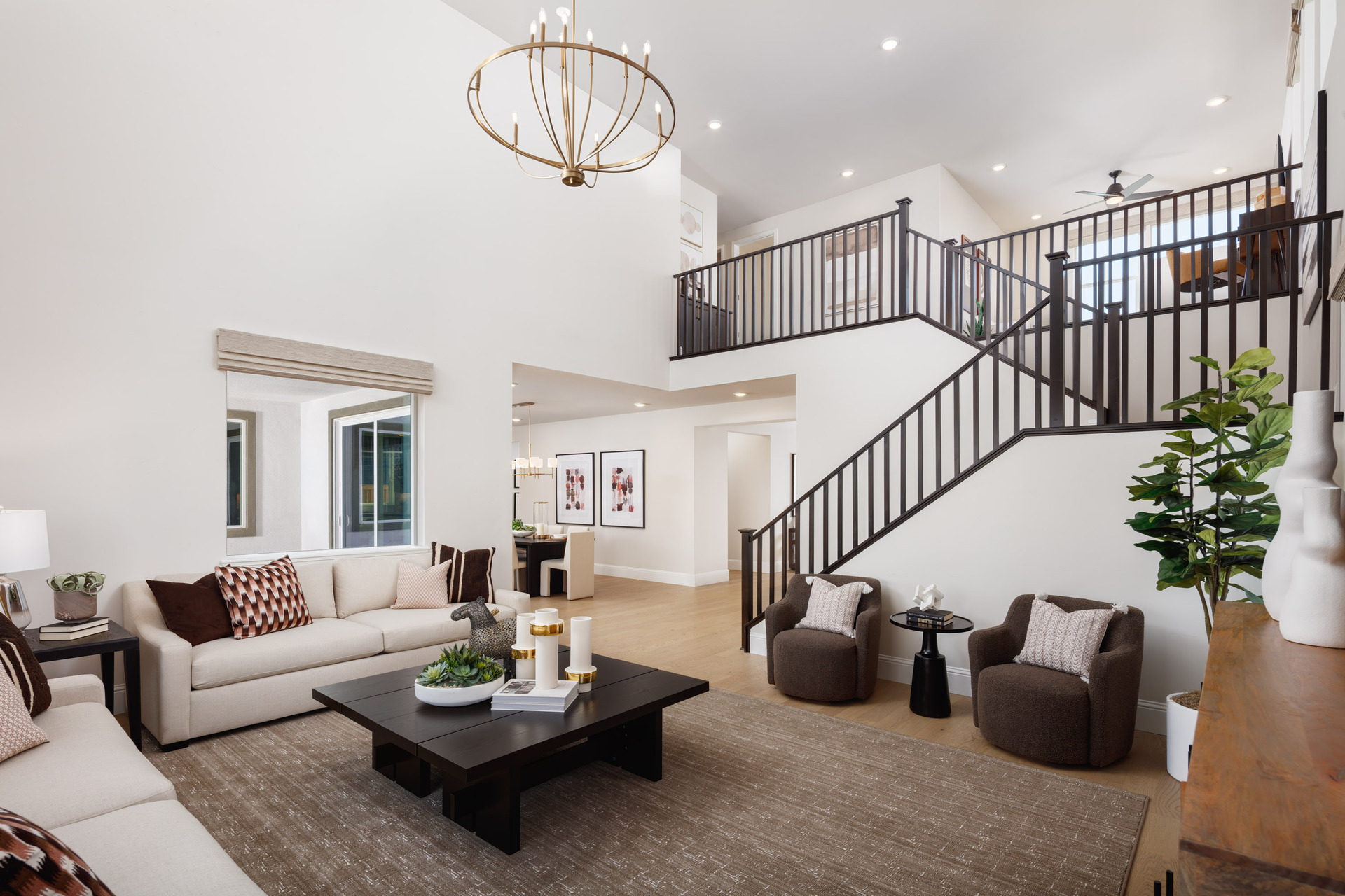 great room with two-story volume ceiling, wood floors, dark wood coffee table, two white sofas, and two brown chairs