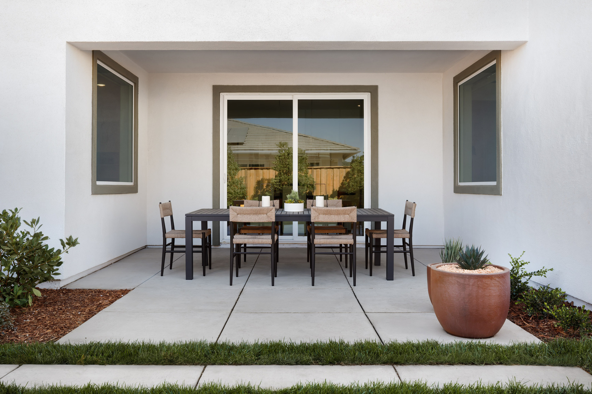 covered back patio with black outdoor table & six rattan chairs, and potted plants