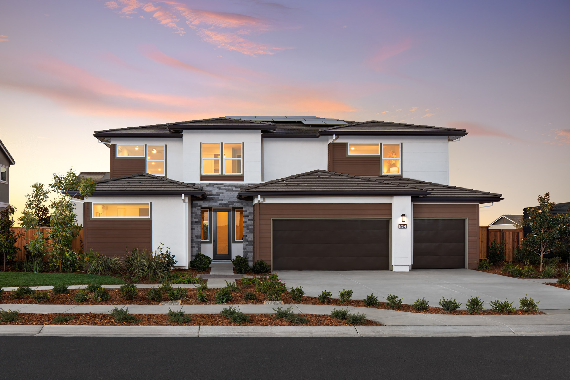 front exterior of two-story brown & white contemporary home with 3-car garage, and solar panels on roof