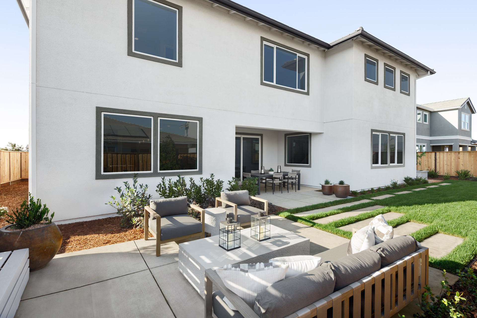 backyard with grassy area, wood & gray outdoor furniture, potted plants, and covered patio