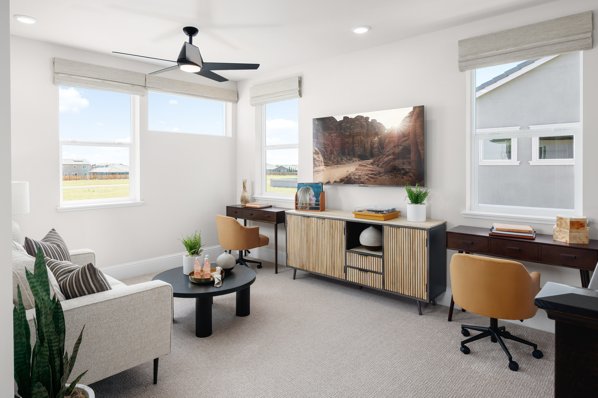 loft with two dark wood desks & gold upholstered swivel chairs, multiple windows, white sofa, and black coffee table