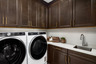 laundry room with espresso upper & lower cabinets, sink, white counters, and white washer & dryer