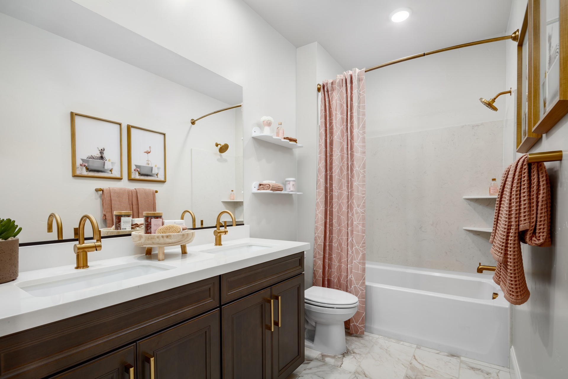 bathroom with espresso cabinets, white counters, two sinks with brushed gold faucets, pink shower curtain & towels, and tub with shower overhead