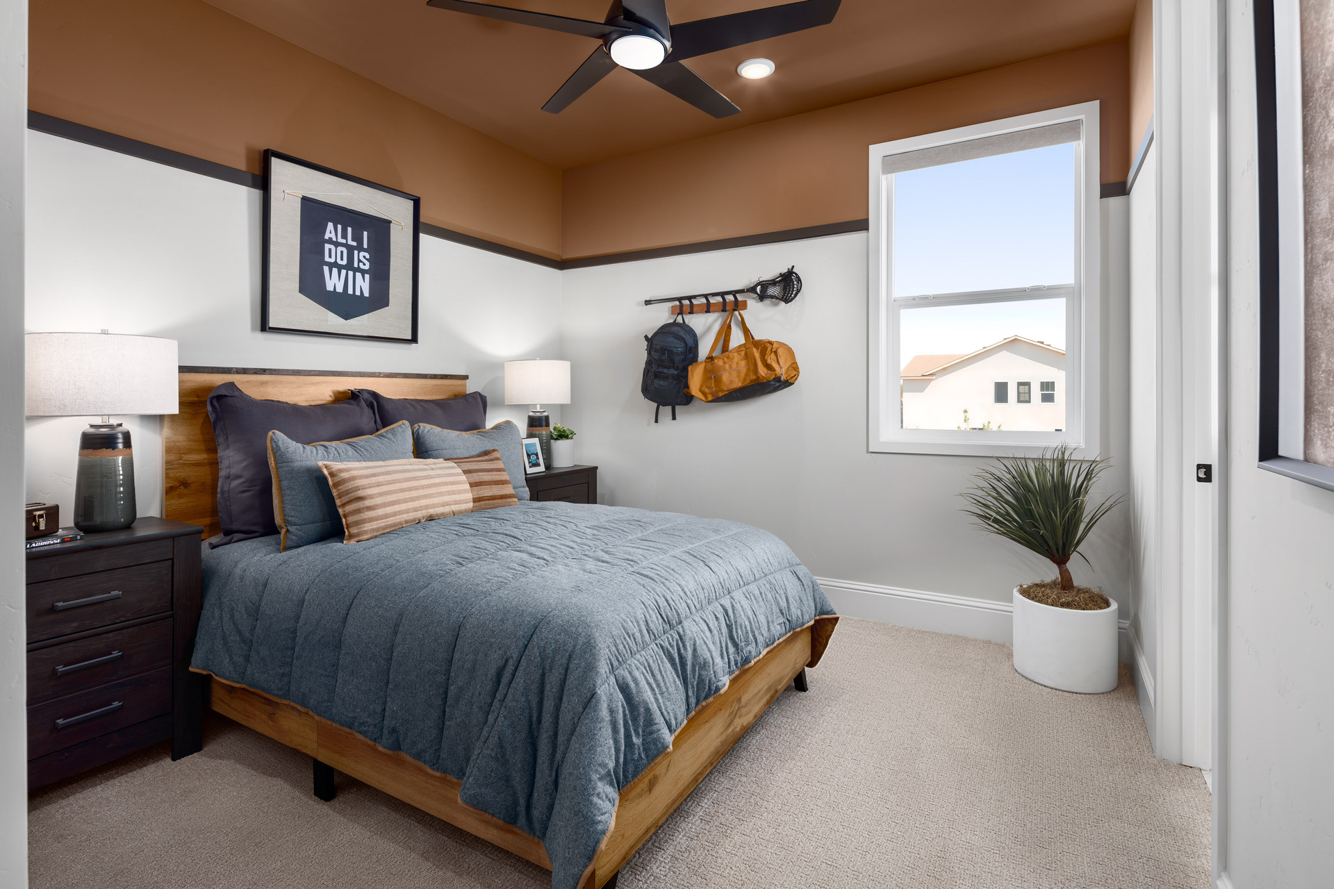 bedroom with rust-colored painted ceiling & sports theme, window, denim blue bedding, wood bed, and potted plant in corner 