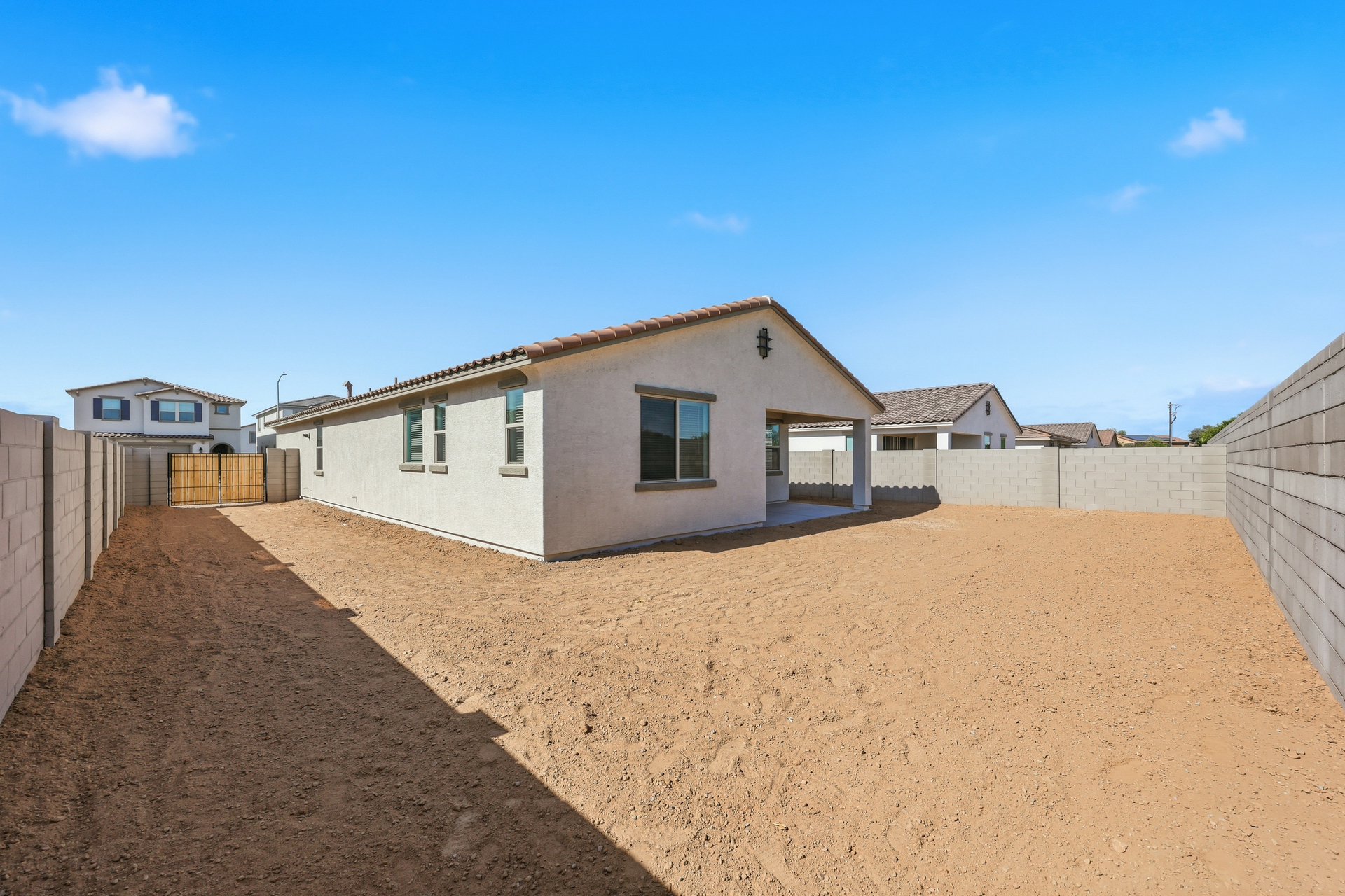 spacious dirt backyard with a double gate, covered patio, and concrete block wall