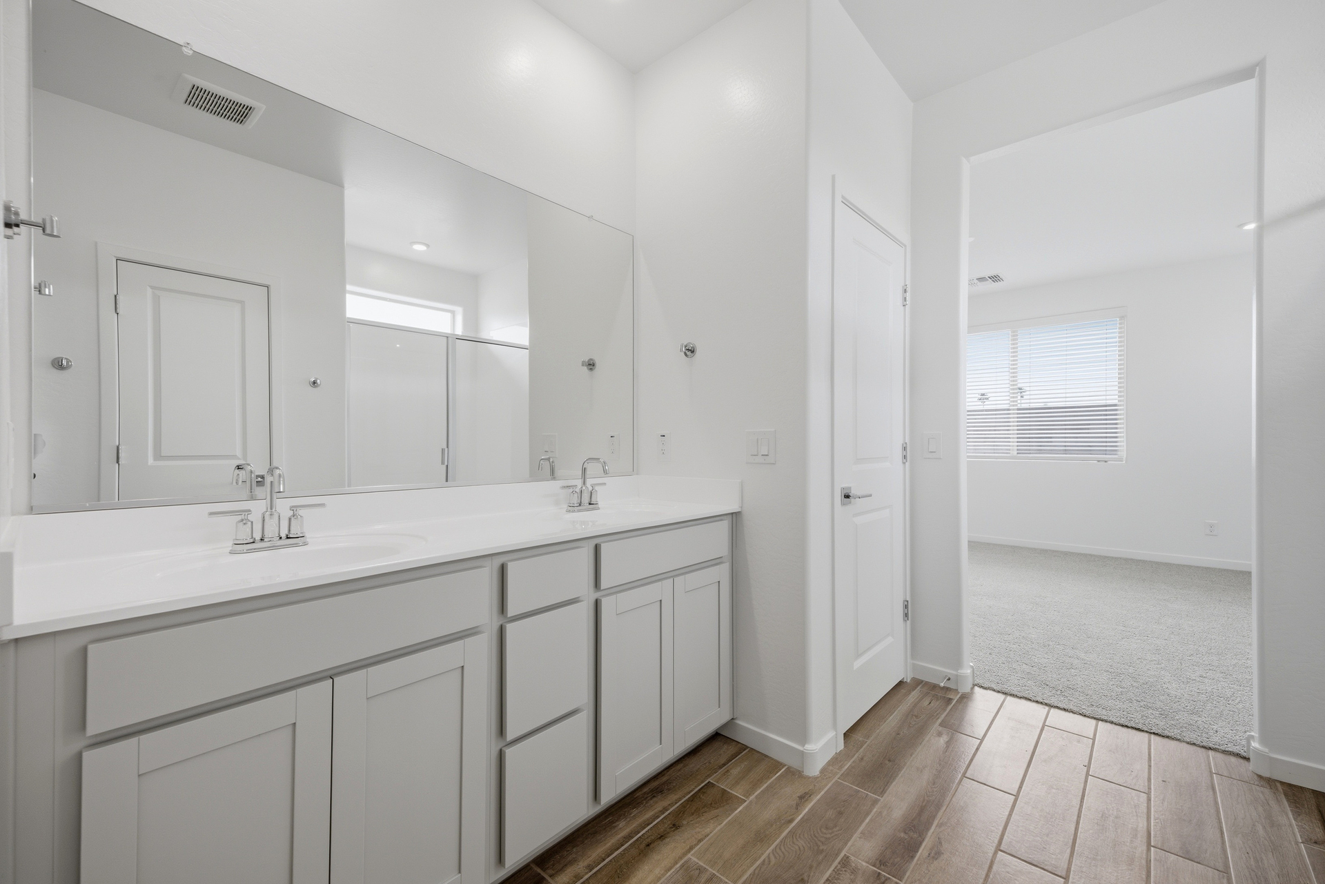 spacious bathroom with grey cabinets, double sink, and chrome faucets
