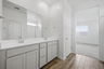 spacious bathroom with grey cabinets, double sink, and chrome faucets