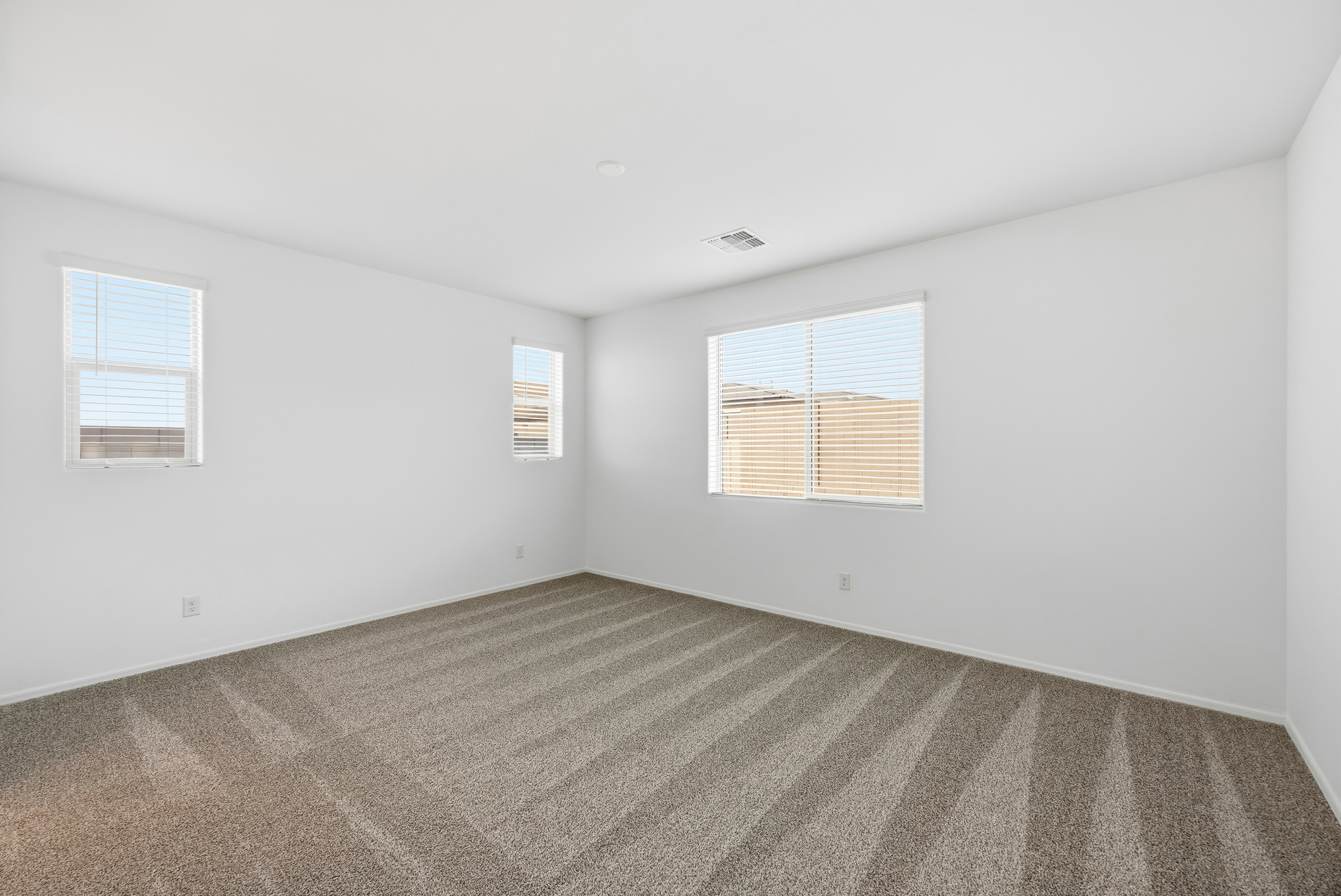 spacious bedroom with light brown carpet and windows for natural light