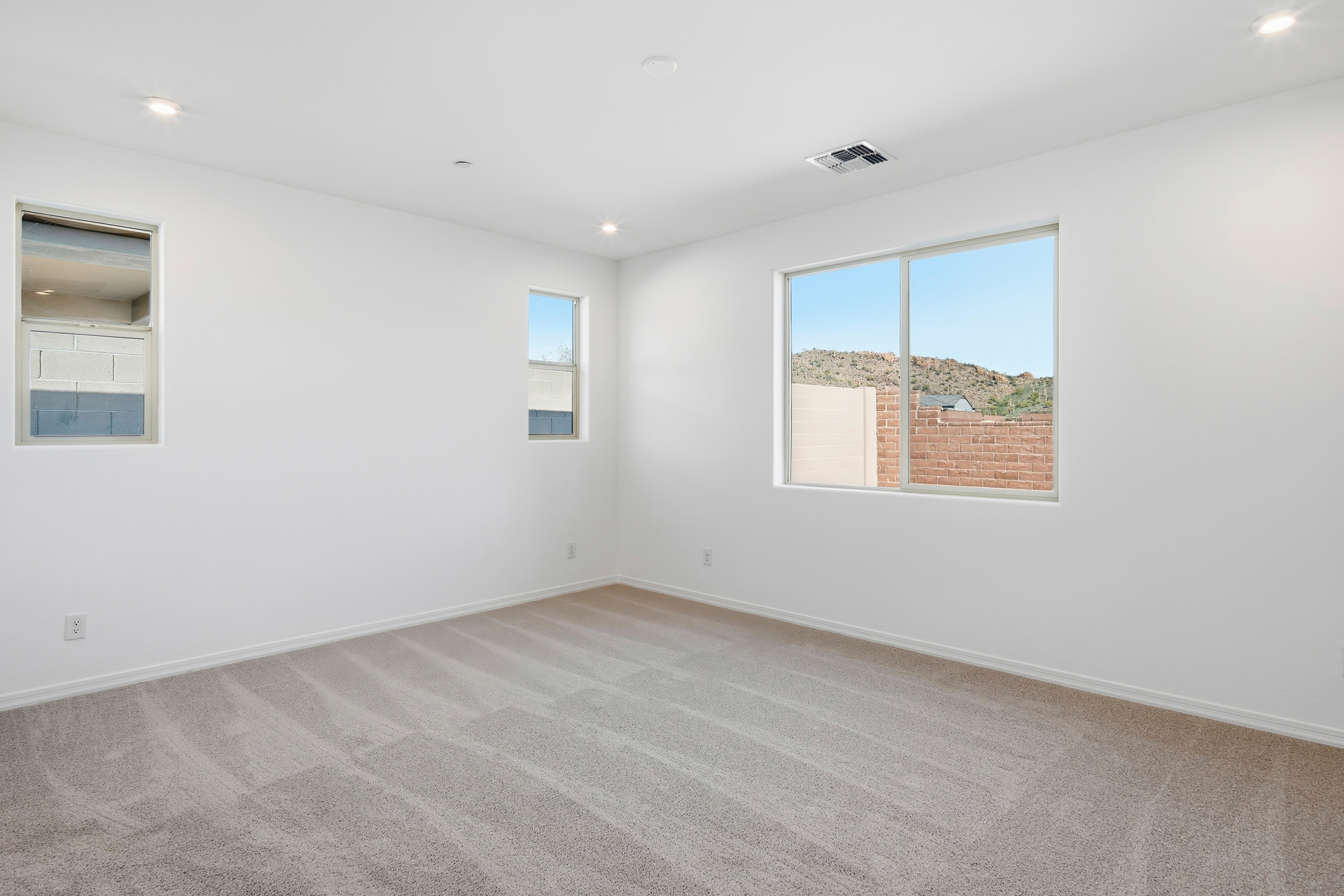 spacious bedroom with light brown carpet and windows for natural light