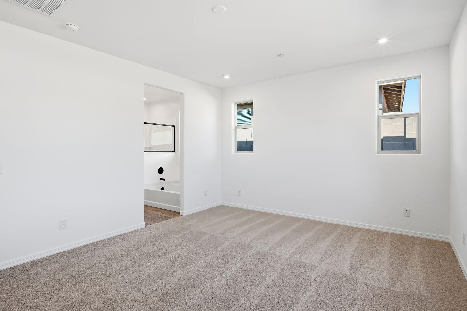 spacious bedroom with light brown carpet and windows for natural light
