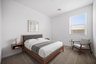 bedroom with a large walnut bedframe, floating walnut nightstands, and a grey accent chair