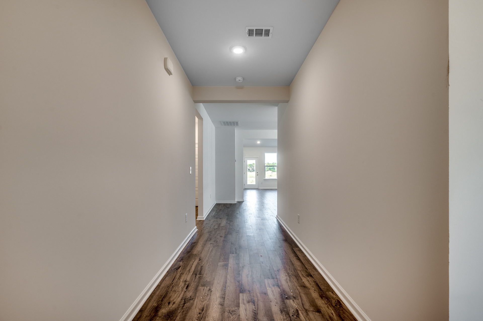 welcoming hallway with tan walls, puck lighting and hardwood flooring throughout