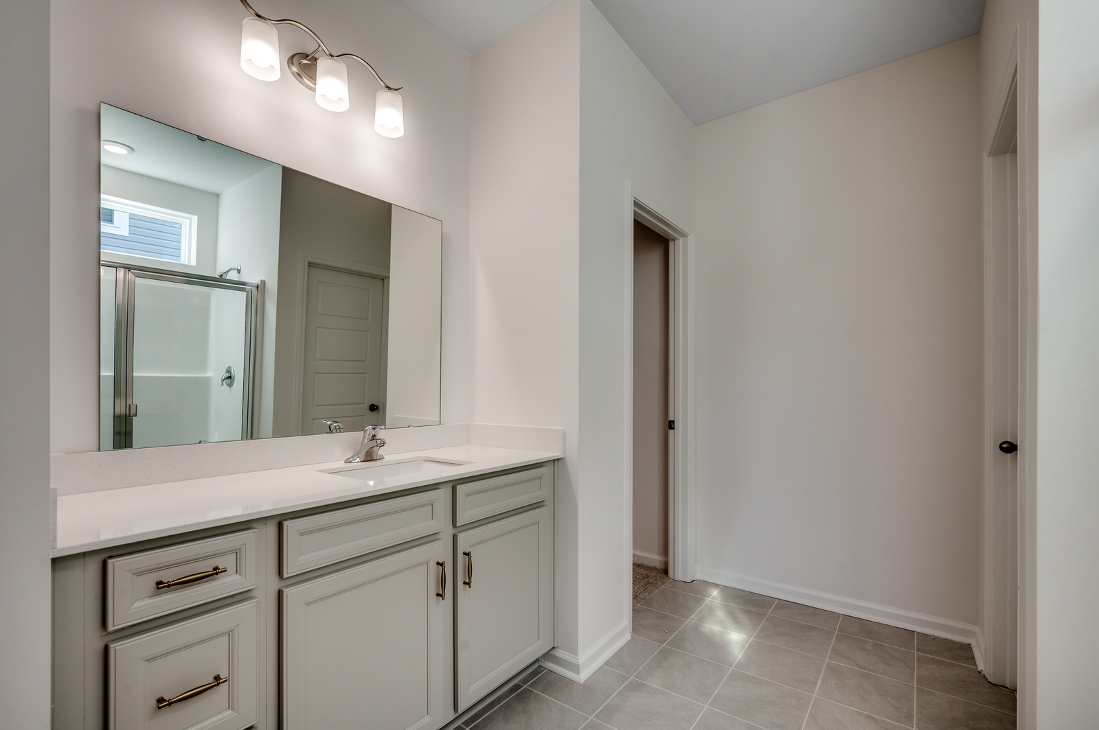 large single sink vanity with gray cabinets, gold hardware and tile flooring throughout
