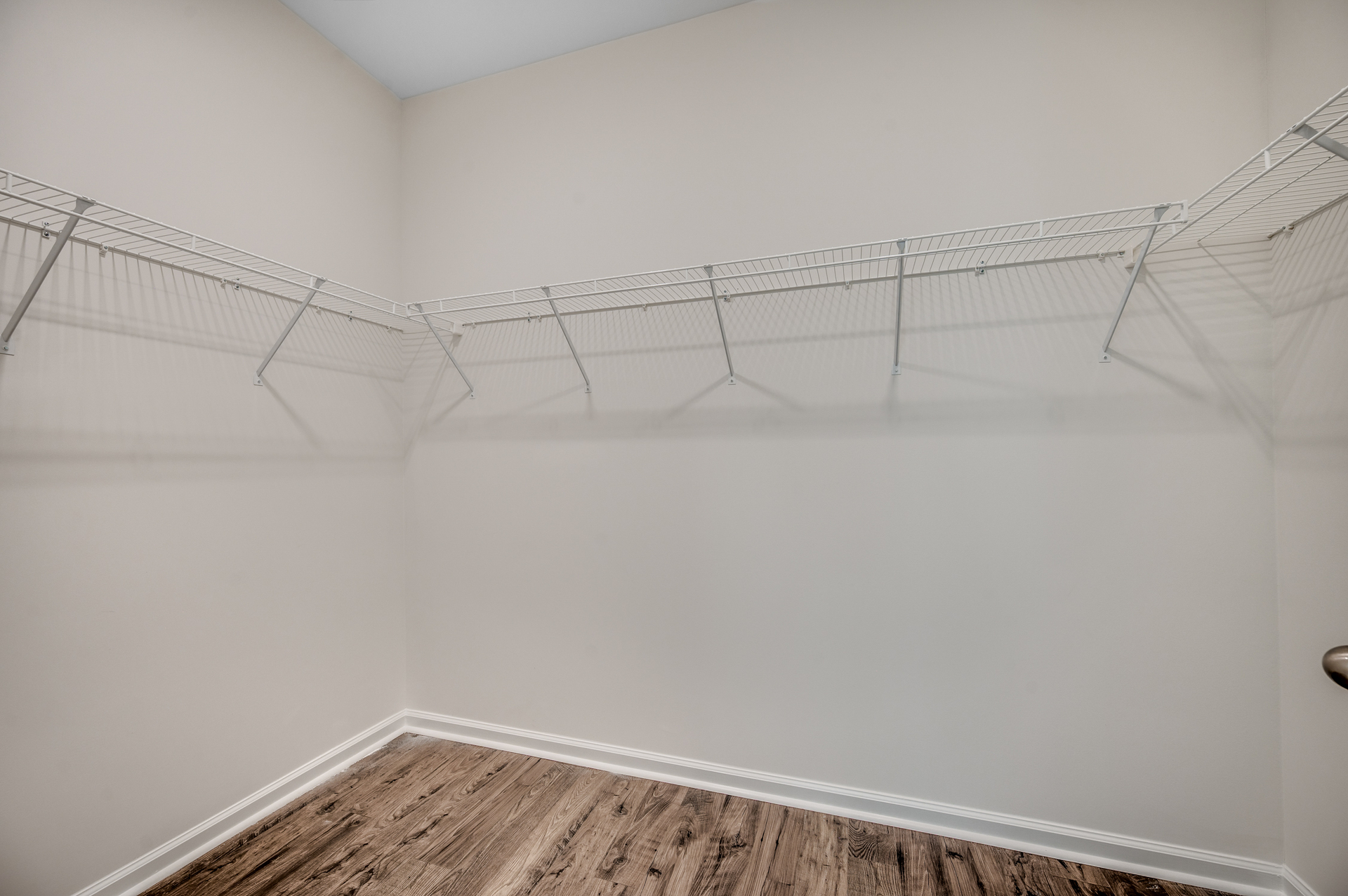 spacious walk-in closet with white wire shelving and hardwood flooring