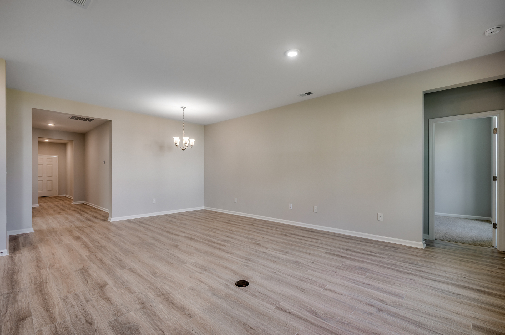 open-concept area with hardwood flooring, tan walls and chandelier 