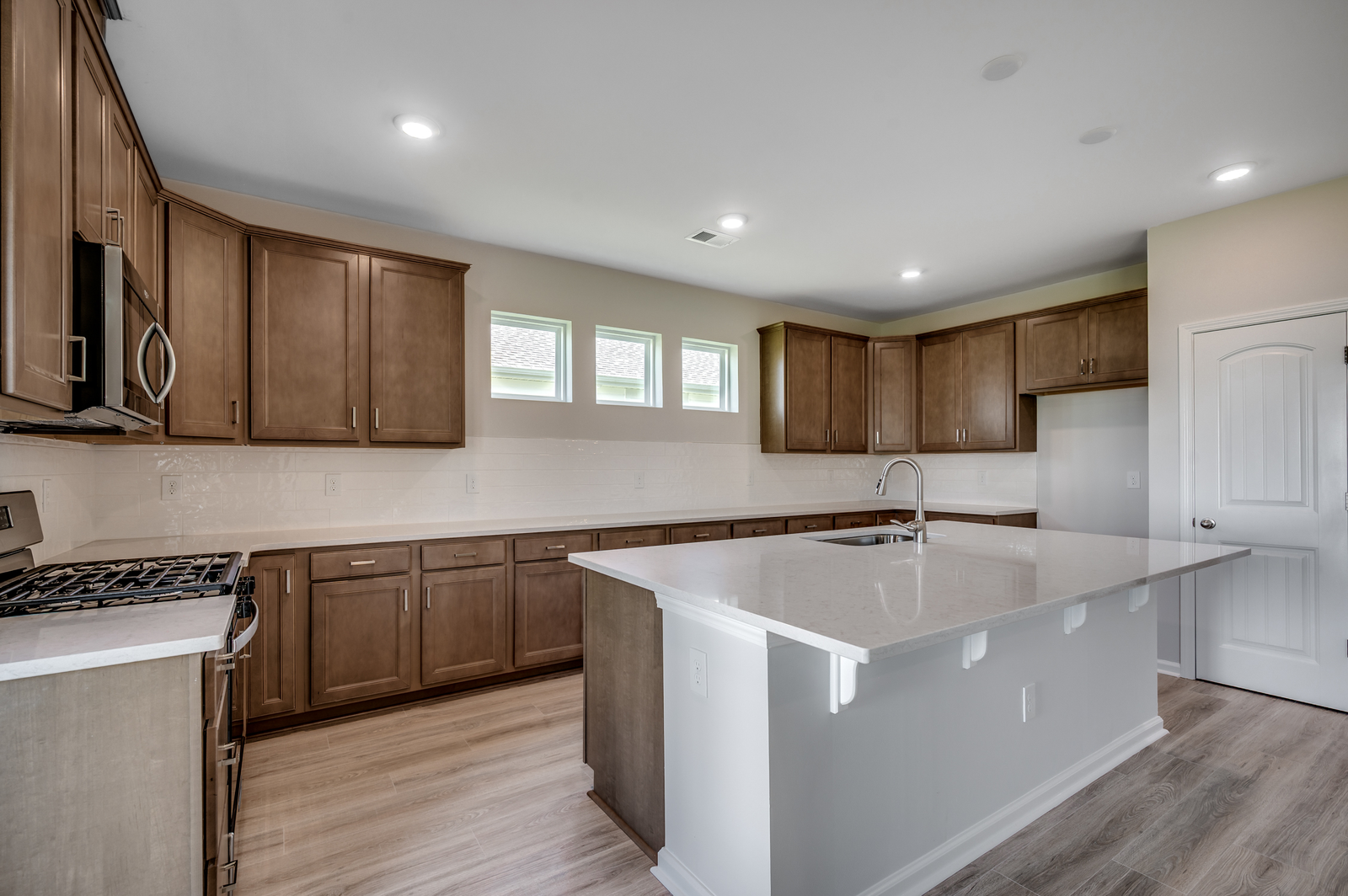 dark brown cabinets with large island, bright white countertops and windows for natural lighting